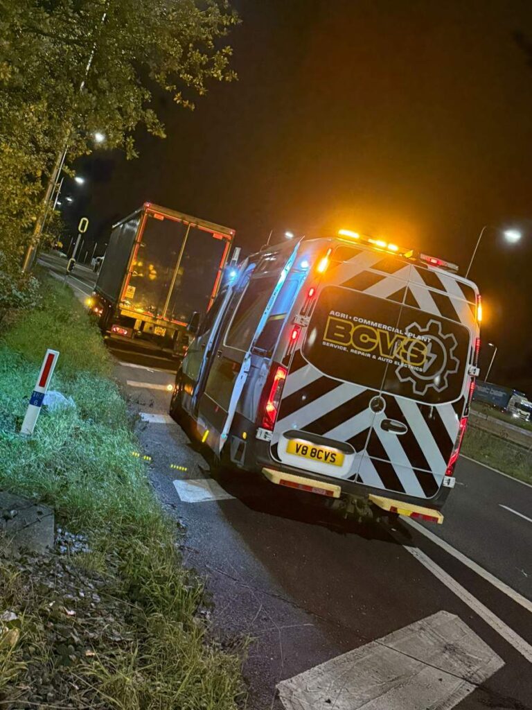 BCVS van with beacons working behind an articulated trailer on a lit road at night