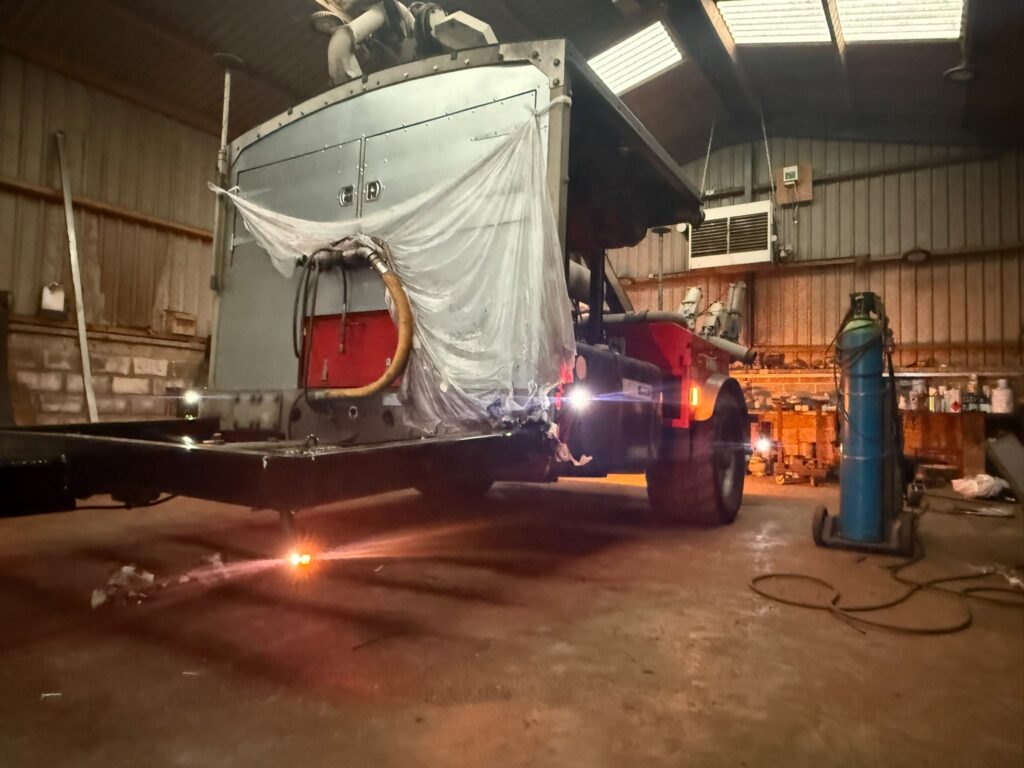 Tanker body on a chassis inside a workshop, part sheeted, with new marker and rear lights wired in and illuminated