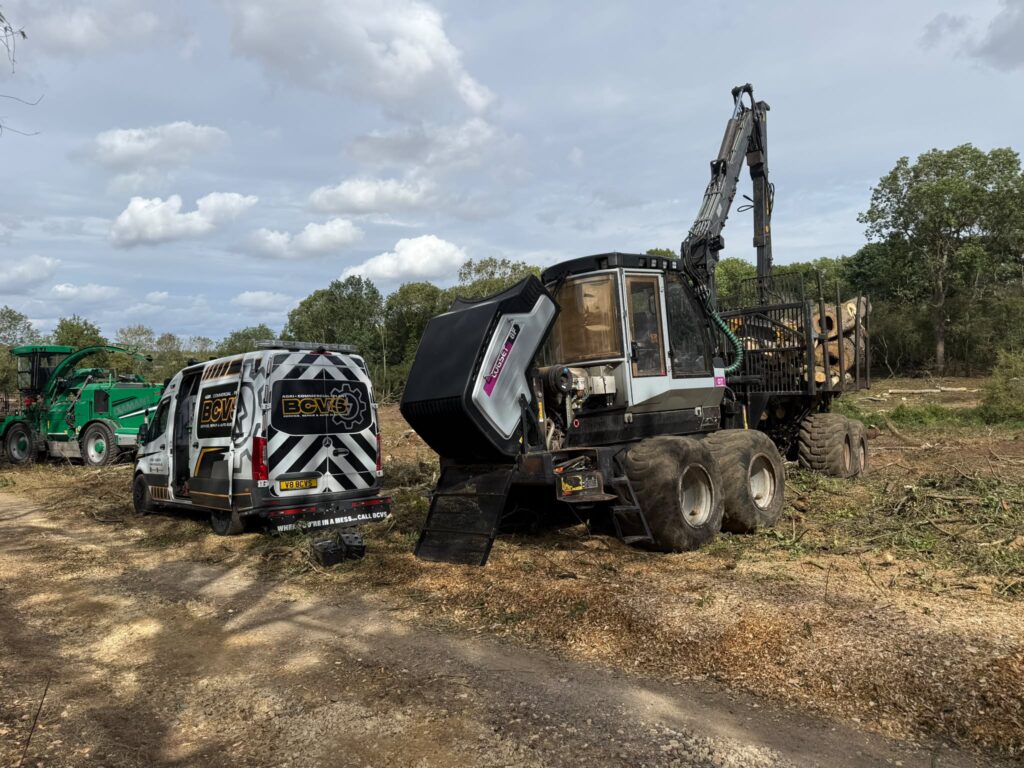 BCVS van alongside a tracked forestry forwarder loaded with timber at a woodland clearance site, engine cover raised for repair