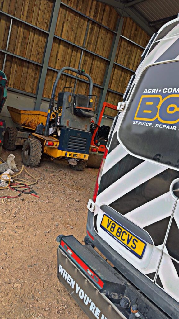 Rear of the BCVS van inside a farm shed next to a yellow site dumper, with cables and equipment laid out on the floor